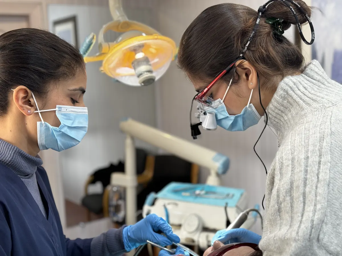 Two clinicians in masks, one wearing magnifying loupes, treating a patient at the practice.